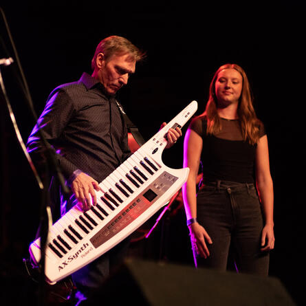 Keytar player standing with singer while they both look out from stage.