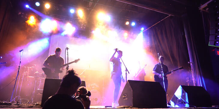 Band performs on stage at Eco Jam. Singer and two guitarists are backlit.