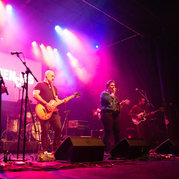 A band backlit in red, blue and purple spotlight on the stage, singing and playing guitars.
